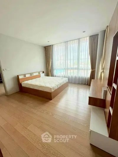 Spacious bedroom with large window and wooden flooring in modern apartment.