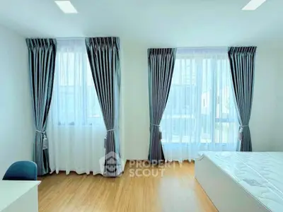 Bright bedroom with large windows and elegant curtains, featuring a comfortable bed and wooden flooring.