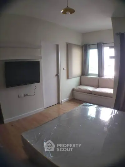 Cozy bedroom with natural light, featuring a wall-mounted TV and a comfortable seating area by the window.
