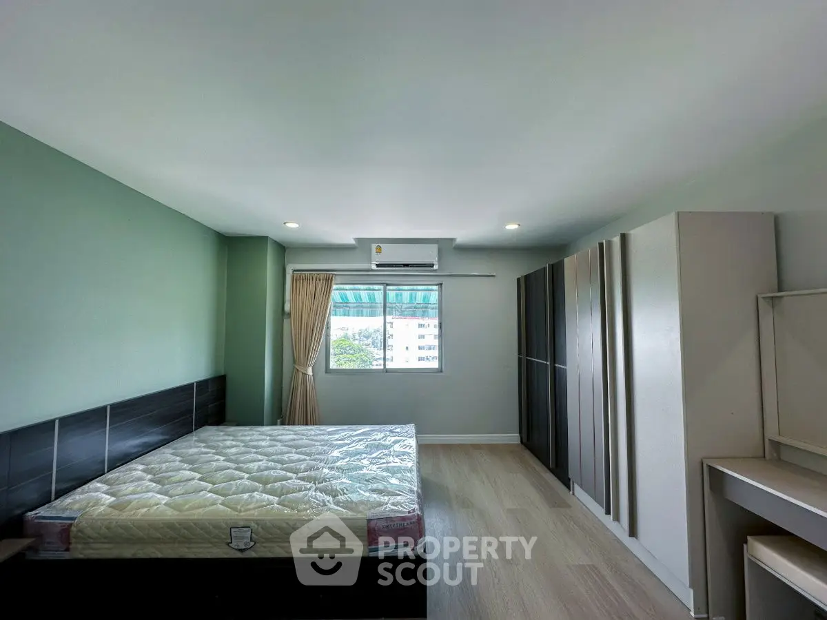 Spacious bedroom with large window and modern furnishings, perfect for comfortable living.