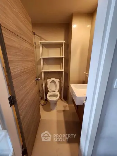 Compact bathroom with modern fixtures and wooden door, featuring a white toilet and sink.