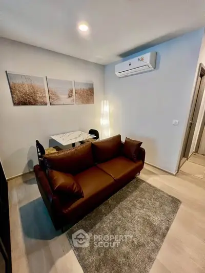 Cozy living room with brown sofa, wall art, and air conditioning unit.