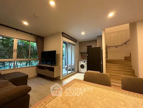 Modern living room with open kitchen and staircase, featuring a washing machine and cozy seating area.