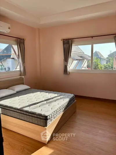Bright bedroom with large windows and wooden flooring, offering a cozy and inviting atmosphere.