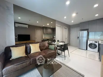 Modern living room with leather sofa, dining area, and kitchen featuring washing machine and sleek cabinetry.