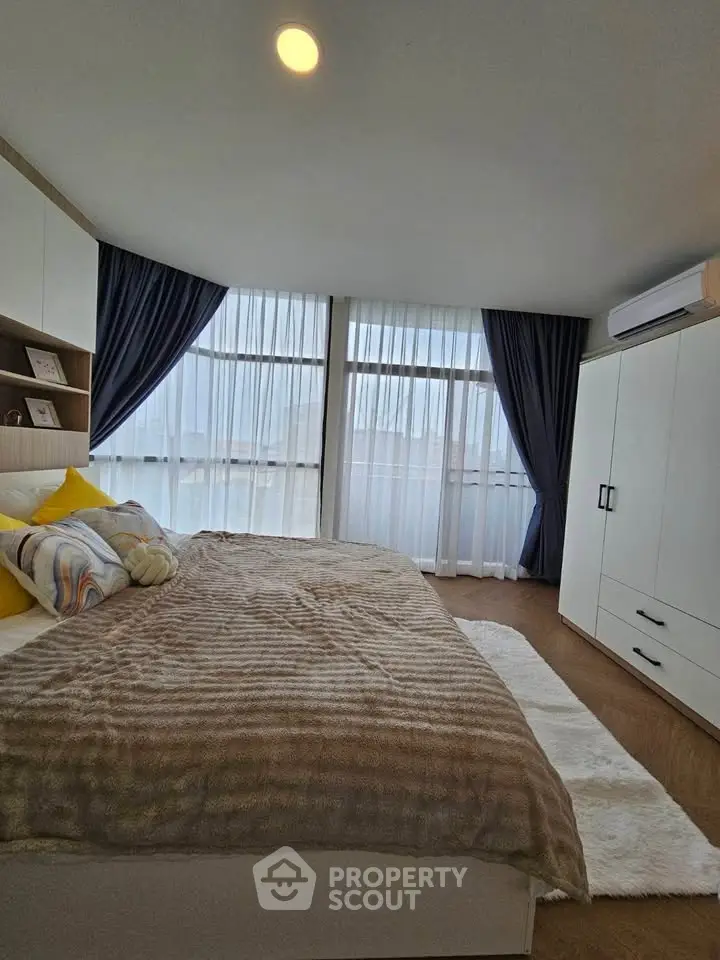 Modern bedroom with large windows, cozy bed, and stylish decor.