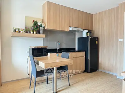 Modern kitchen with sleek wooden cabinets and dining area, featuring a black fridge and stylish decor.