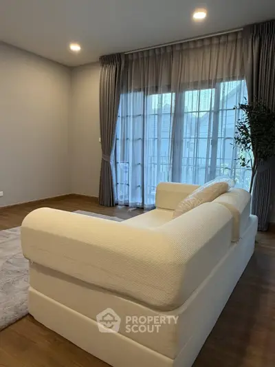 Spacious living room with elegant sofa and large window, perfect for relaxation and natural light.