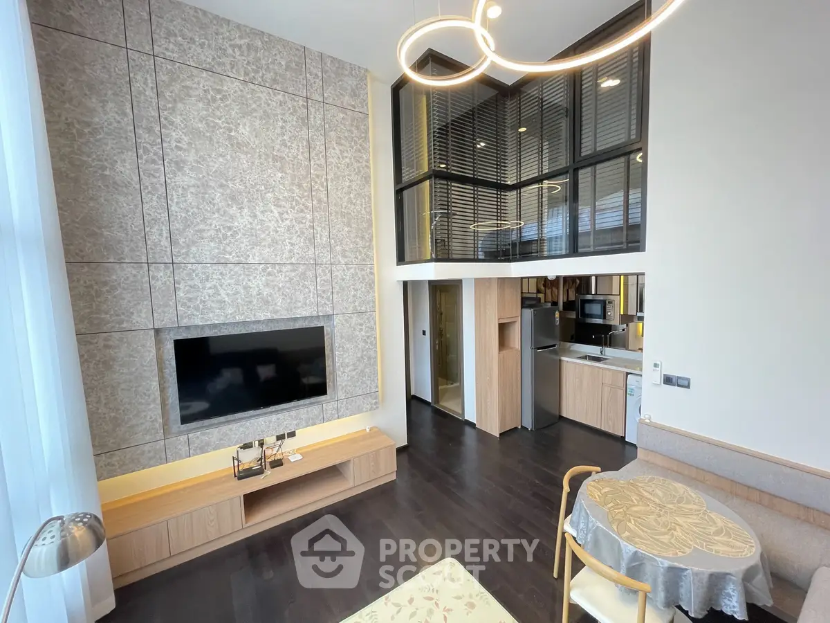Modern living room with high ceiling, stylish lighting, and open kitchen layout in a contemporary apartment.