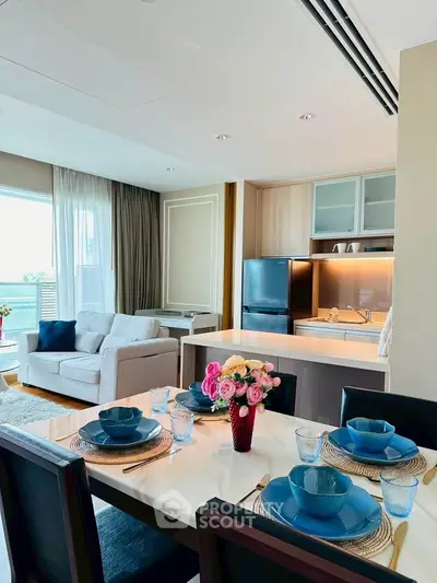 Modern open-plan living room and kitchen with elegant dining setup and natural light.