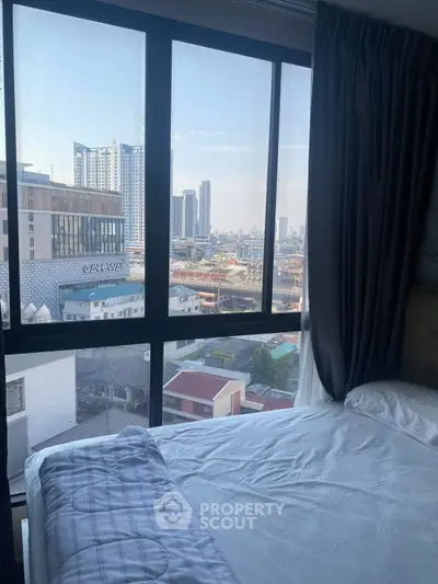 Modern bedroom with city view through large windows, featuring cozy bedding and stylish curtains.
