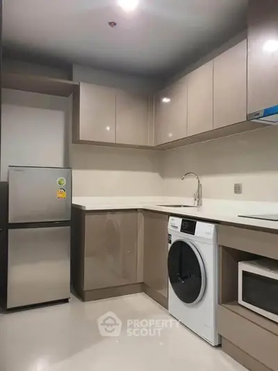 Modern kitchen with sleek cabinetry, washing machine, and microwave in a compact layout.