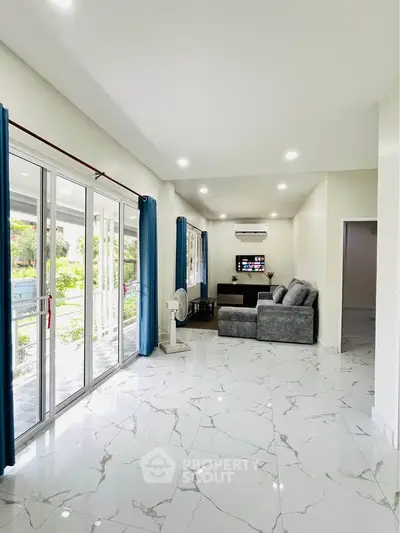 Spacious living room with marble flooring and large windows offering garden views.