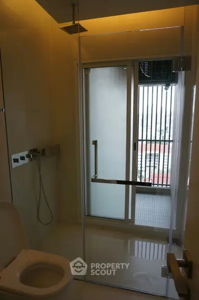 Modern bathroom with glass shower and city view balcony access.