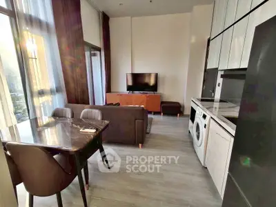 Modern living room with open kitchen and washing machine, featuring sleek furniture and large windows.
