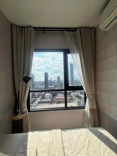 Cozy bedroom with city view through large window, modern decor and natural light.