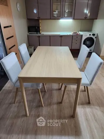 Modern kitchen with wooden dining table and chairs, featuring sleek cabinets and a washing machine.