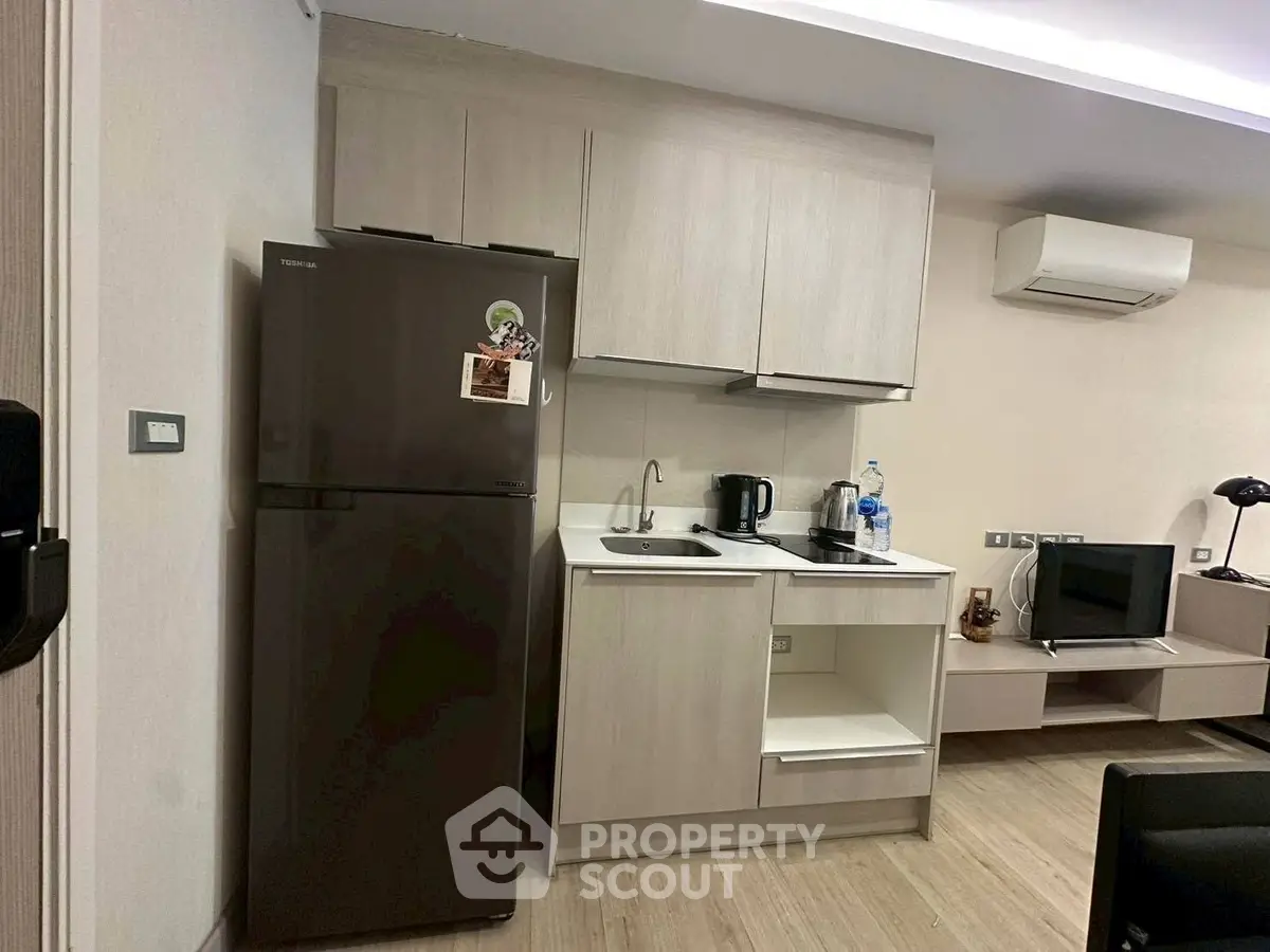 Modern compact kitchen with fridge and sleek cabinetry in cozy apartment