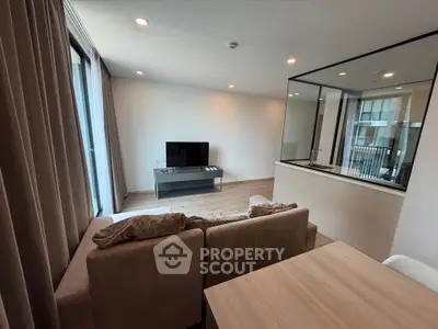 Modern living room with cozy sofa and TV, featuring large windows and elegant decor.