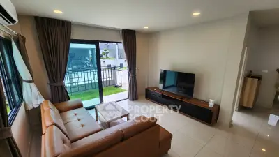 Modern living room with leather sofa and TV, opening to a balcony with a view.