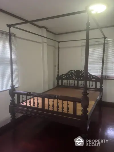 Elegant bedroom featuring a vintage four-poster bed, polished wooden floors, and ample natural light from large windows with blinds.