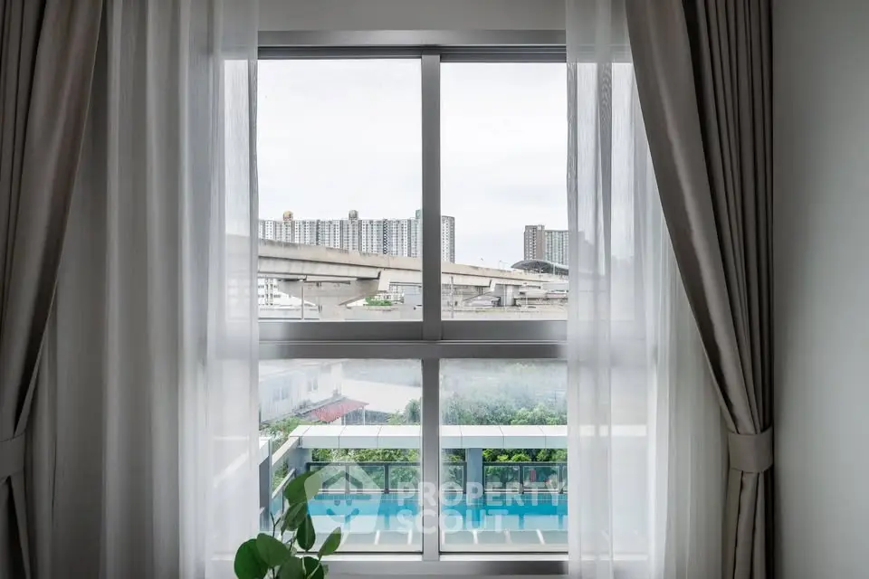 Modern apartment window view with cityscape and pool, featuring elegant curtains and urban living.
