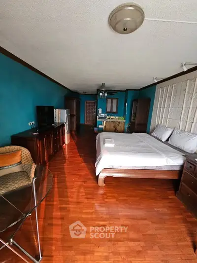 Spacious bedroom with wooden flooring and teal walls, featuring a cozy bed and modern furniture.