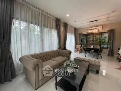 Elegant living room with plush sofa and dining area, featuring large windows and stylish decor.
