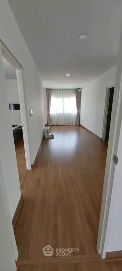 Spacious empty room with wooden flooring and large window, ideal for customization.
