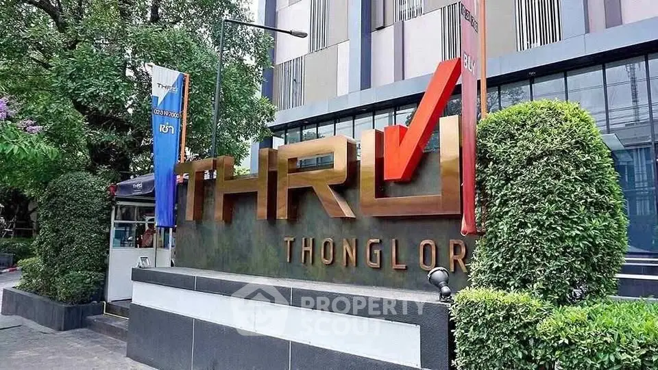 Modern building exterior with stylish signage at Thonglor, surrounded by lush greenery.
