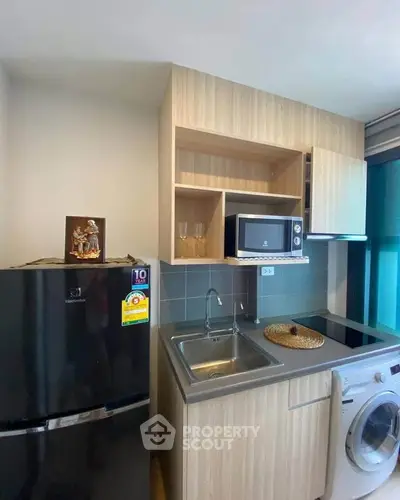 Modern compact kitchen with fridge, microwave, and washing machine in stylish apartment.