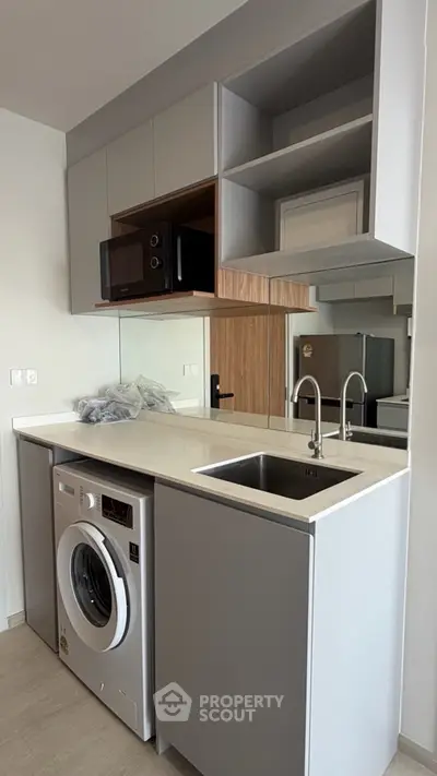 Modern compact kitchen with built-in washing machine and microwave, sleek cabinetry, and stainless steel sink.
