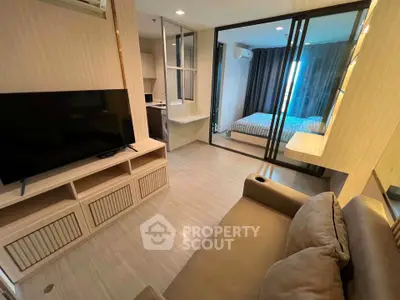 Modern living room with TV and cozy sofa, adjacent to a stylish bedroom with glass partition.