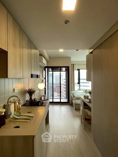Modern apartment interior with open kitchen and cozy living area leading to a balcony with city view.