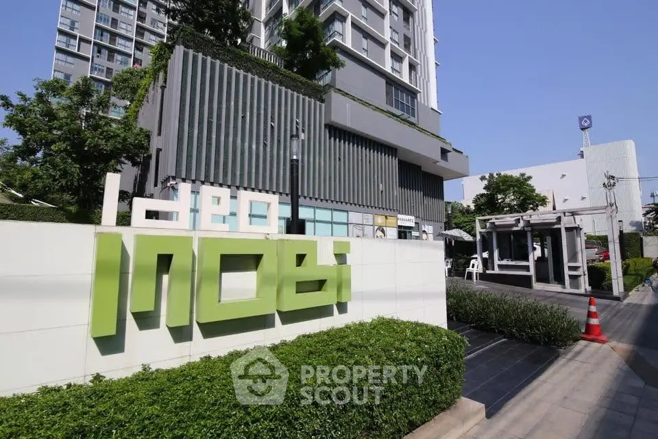 Modern condominium building exterior with lush greenery and clear blue sky.