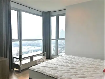 Bright bedroom with large windows offering a stunning city view, featuring a comfortable mattress.