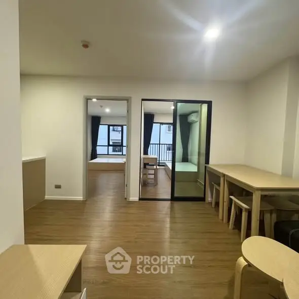 Modern apartment interior with open layout and wooden flooring, featuring a dining area and view into a bedroom.