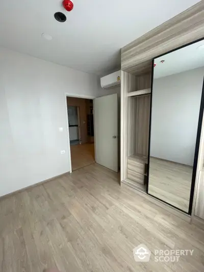 Modern empty bedroom with wooden flooring and built-in mirrored wardrobe