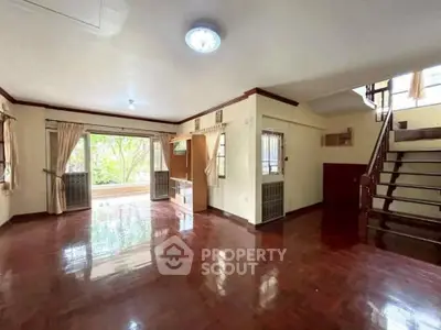 Spacious living room with wooden flooring and large windows offering natural light and garden view.