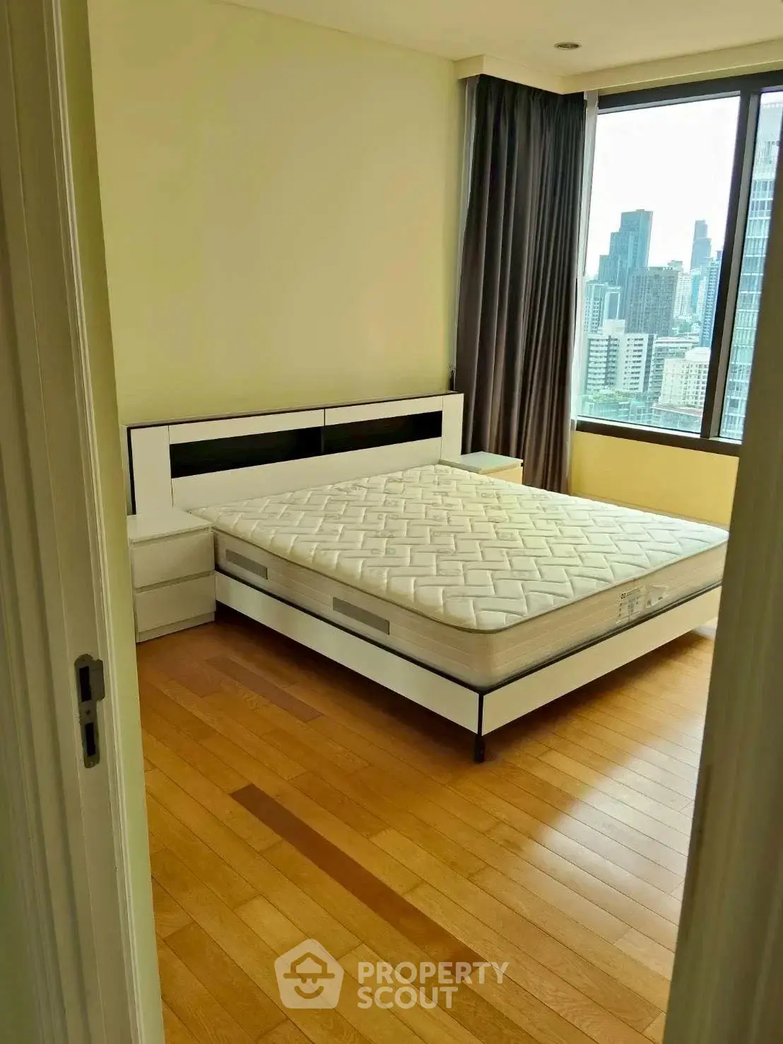 Spacious bedroom with city view and modern furnishings in high-rise apartment.