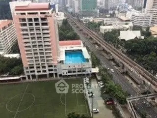 High-rise building with rooftop pool and cityscape view, adjacent to sports field and railway.