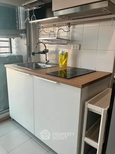Compact modern kitchen with sleek white cabinets and electric cooktop, ideal for urban living.