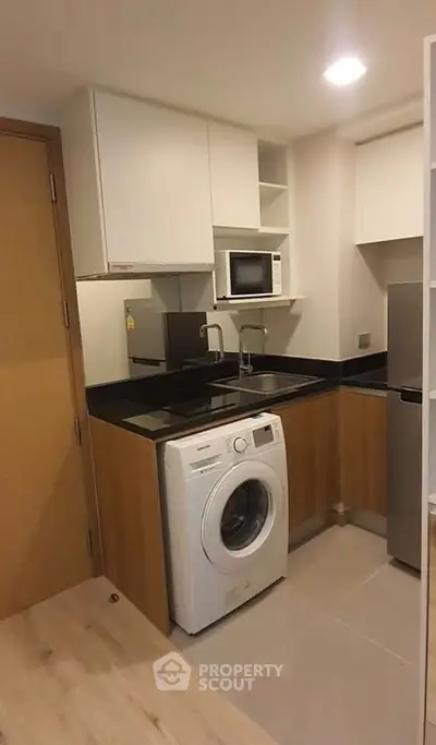 Modern compact kitchen with washing machine and microwave in stylish apartment.