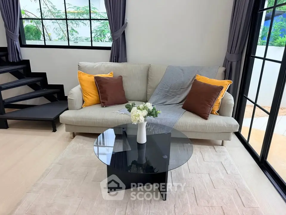 Modern living room with stylish sofa and glass coffee table, featuring large windows and elegant decor.