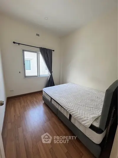 Cozy bedroom with wooden flooring and natural light from window.