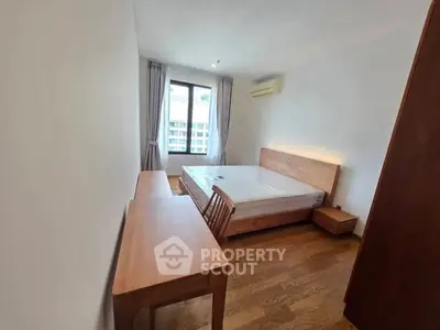 Spacious bedroom with wooden furniture and large window offering natural light.