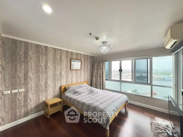 Spacious bedroom with large windows offering stunning river views, featuring elegant wood flooring and modern decor.