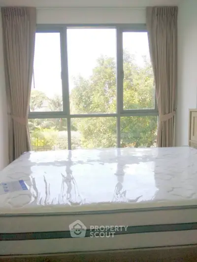 Bright bedroom with large window and garden view, featuring a new mattress.