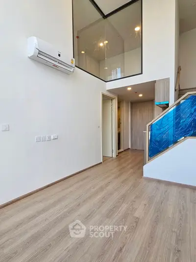 Modern duplex interior with sleek wooden flooring and glass partition, featuring a stylish staircase and air conditioning.