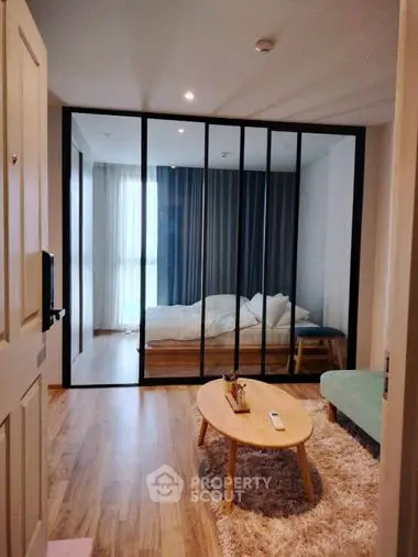 Modern studio apartment with glass partition bedroom, plush area rug, and chic wooden furniture, perfect for urban living.